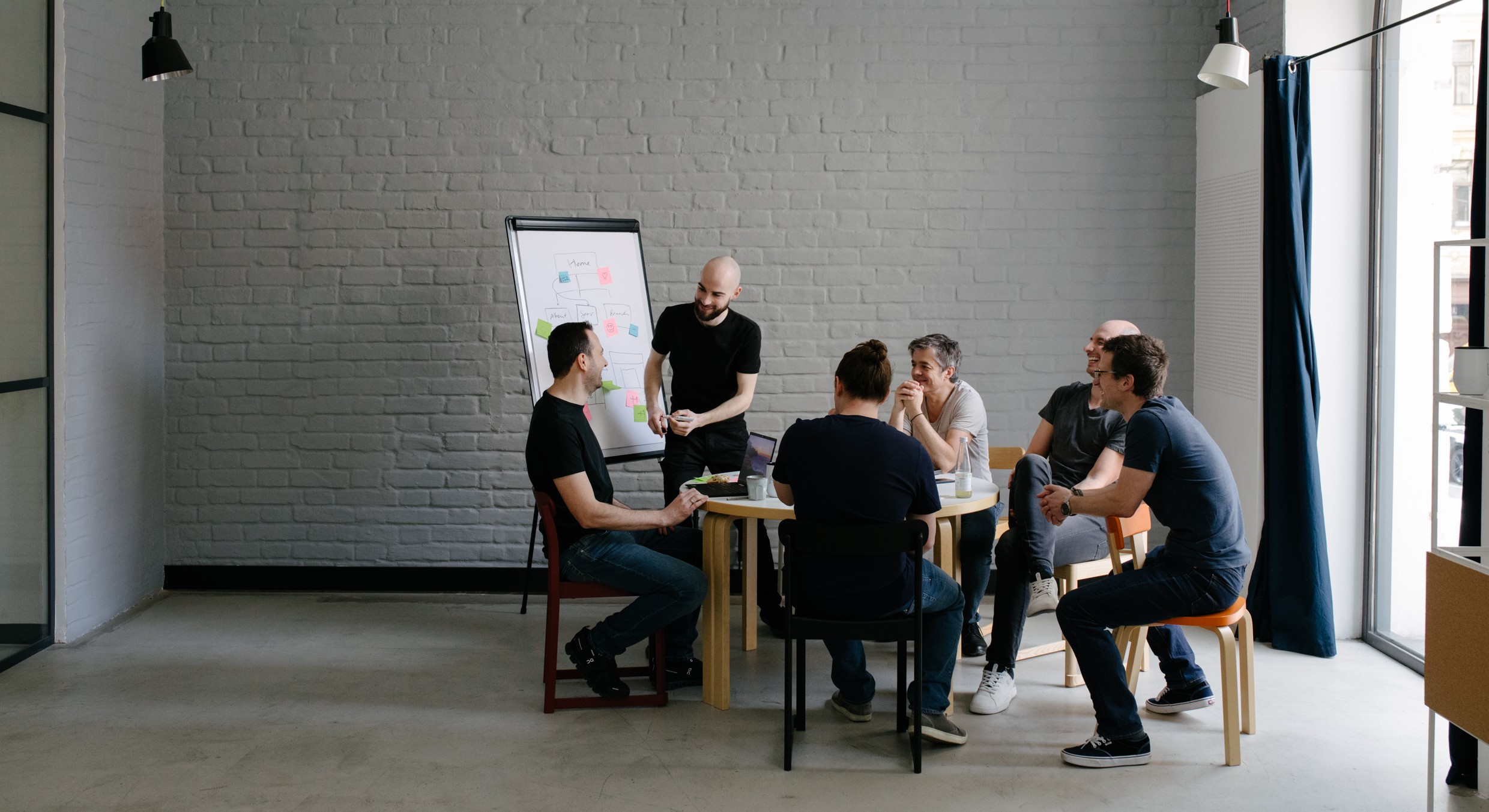 Größeres Team, das um einen Tisch herum sitzt und gerade an einem Projekt mit einem Flipchart arbeitet